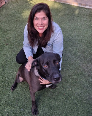 An X-All team member kneeling on the lawn with her black Lab mix