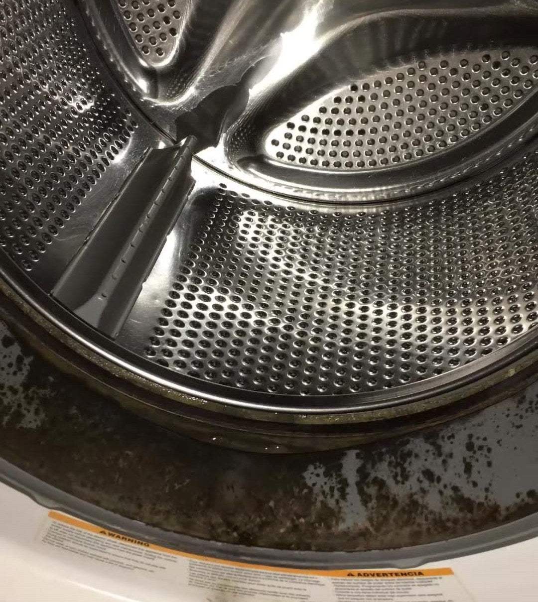 Front-loading washer drum with dark dirt and grime along the bottom of the door seal, before cleaning